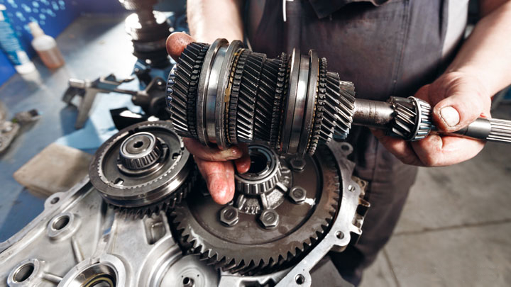 A mechanic holding a Toyota forklift driveshaft with worn gears